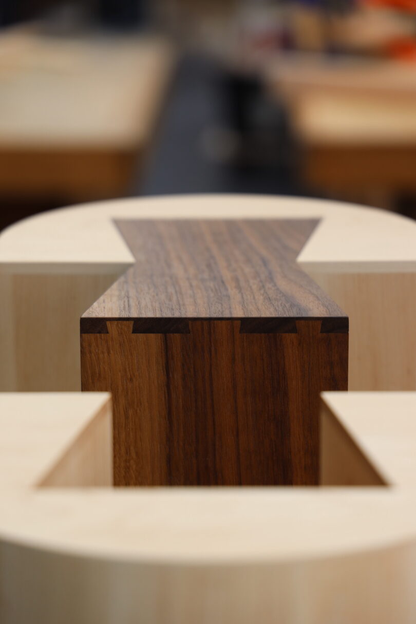 Close-up of a dovetail joint connecting two pieces of wood, showing precise craftsmanship and contrasting light and dark wood tones