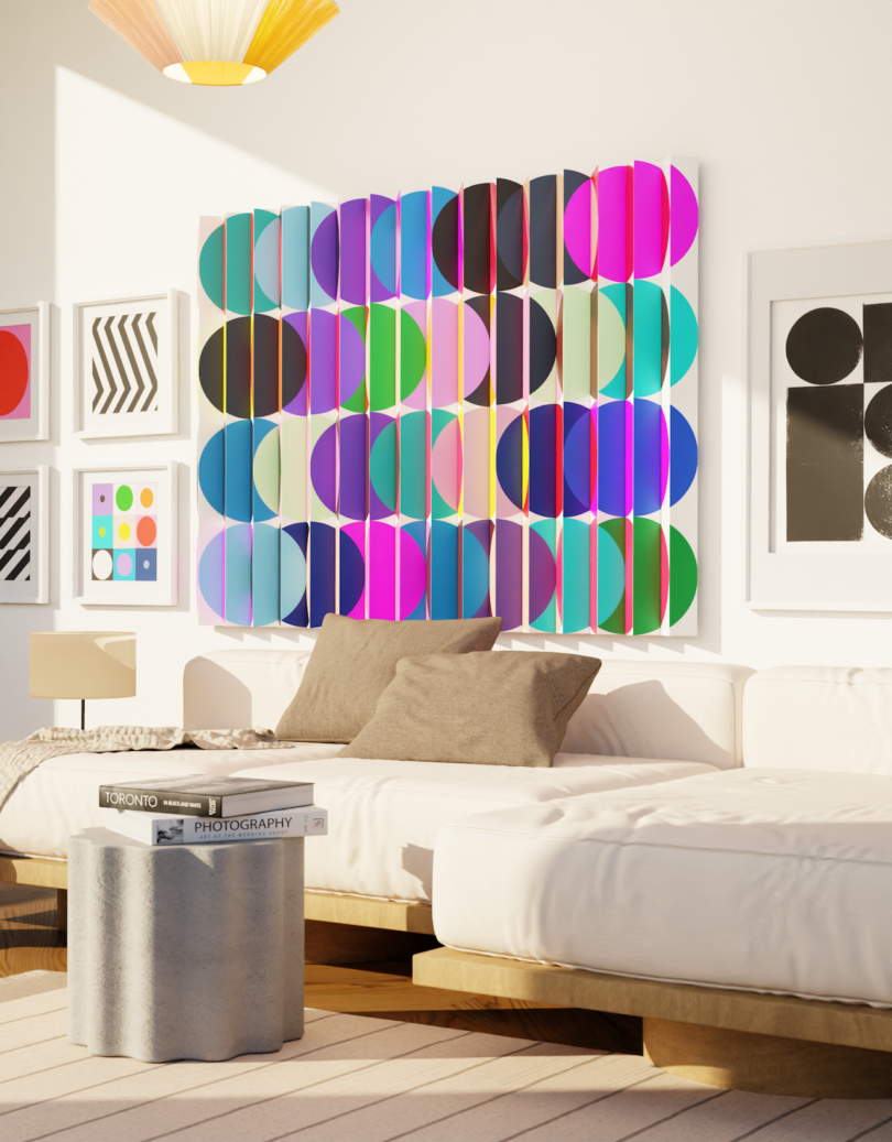 A modern living room with a white sofa, colorful geometric wall art, graphic prints, and a small gray side table with books. Bright sunlight fills the space