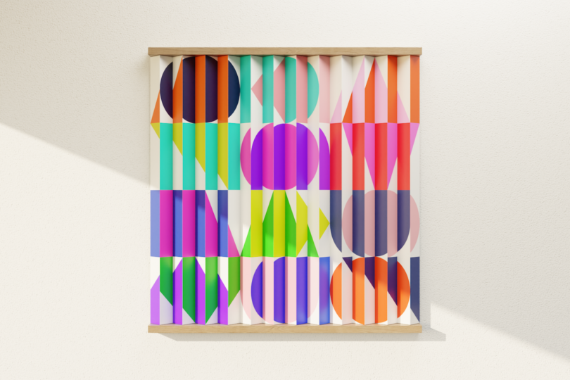 A colorful geometric artwork with vertical slats, featuring circles and triangles in bright shades of orange, purple, blue, pink, and green, mounted on a white textured wall