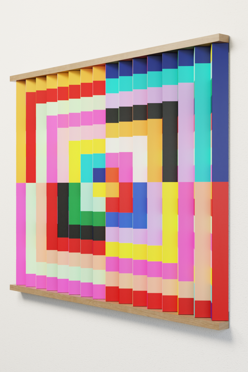 A framed, three-dimensional artwork features vertical strips of colorful, geometric patterns arranged in a concentric square design, mounted on a white wall