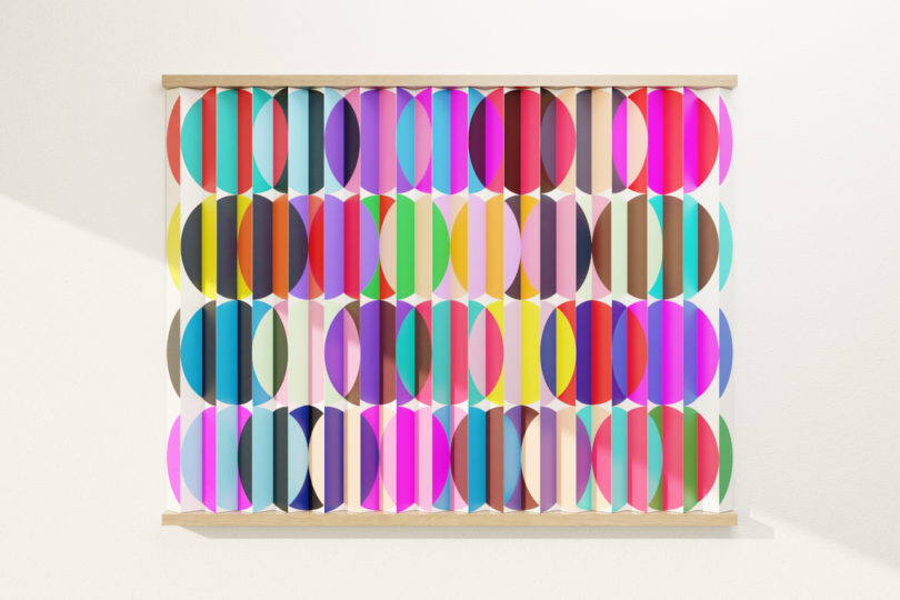 A square artwork featuring rows of colorful, overlapping ovals and vertical stripes, mounted on a white wall, is illuminated by diagonal sunlight