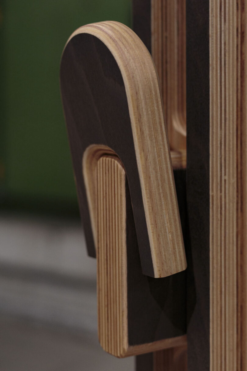 Close-up of a wooden latch mechanism made from layered plywood, attached to a vertical surface with a green background