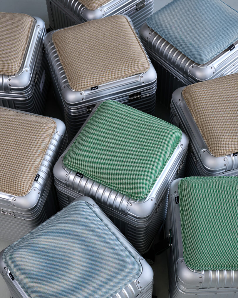 Several metallic cube-shaped stools with textured cushion tops in green, blue, and beige are arranged closely together