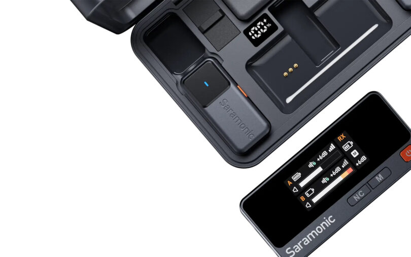 Close-up of the Saramonic Air wireless microphone system with a charging case, transmitter, and receiver displaying audio levels on its screen.