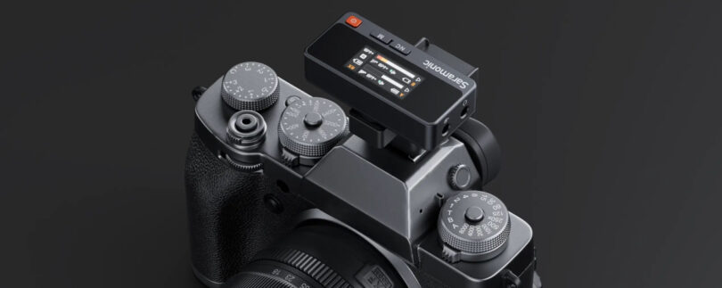 A black Saramonic Air wireless microphone receiver is mounted on top of a digital camera with manual control dials, set against a dark background.