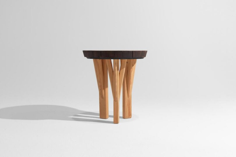A small round table with a dark wooden top and four light-colored, unevenly angled wooden legs, set against a plain white background.
