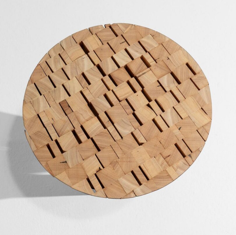 Round wooden tabletop with a geometric, interlocking block pattern, viewed from above against a white background