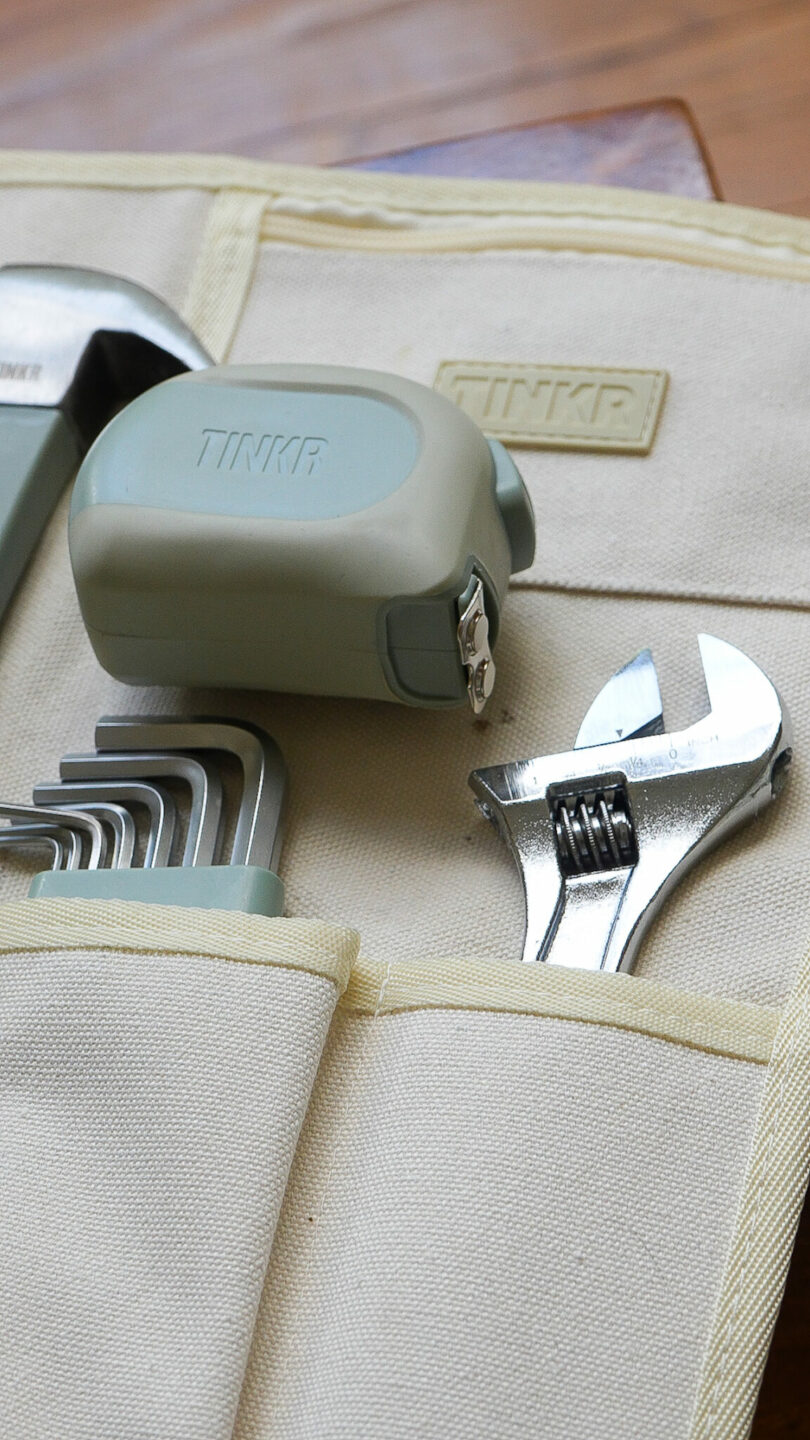 A toolkit pouch containing a tape measure, an adjustable spanner, Allen keys, and part of a wrench, all labeled with the brand "TINKR"