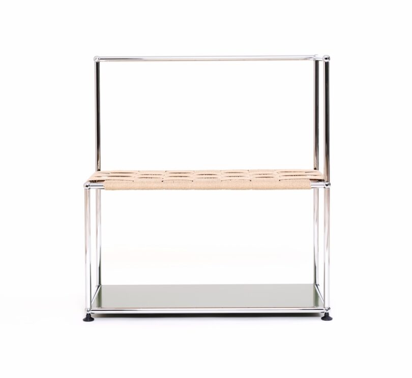 A minimalist shelving unit with a metal frame, a woven rattan middle shelf, and a glass bottom shelf, photographed against a white background.