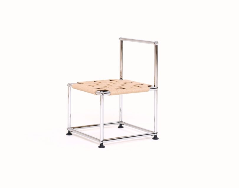 A minimalist chair with a metal frame, woven seat, and partial backrest, displayed against a plain white background.