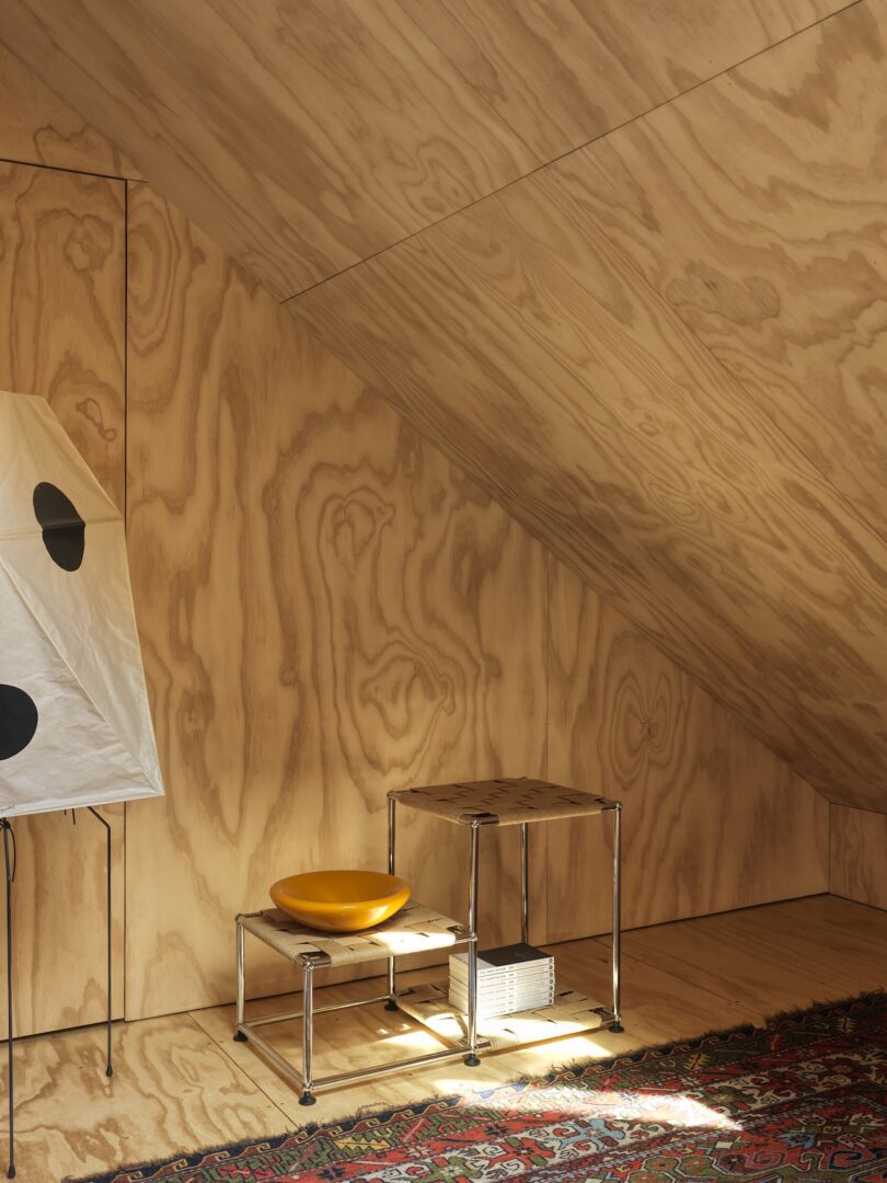 A small corner with plywood walls and ceiling, metal side tables, a yellow bowl, a rug, and a white lamp with black dots.