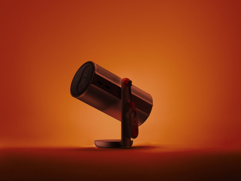 A cylindrical electronic device, possibly an XGIMI portable projector or speaker, is mounted on a stand against an orange gradient background.