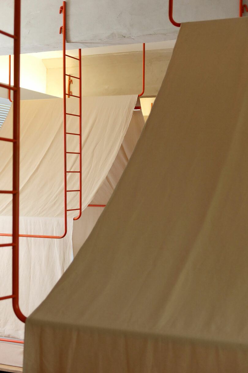 Rows of beige canvas bunk beds with red metal ladders in a well-lit indoor space.
