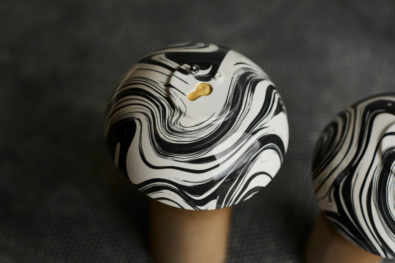 Close-up of a round object with a black and white marbled pattern and a small hole on top, resting on a cylindrical base against a textured background.