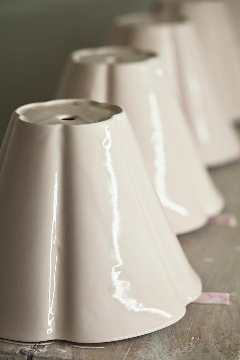 A row of glossy, light-colored ceramic lamp shades placed upside down on a surface.