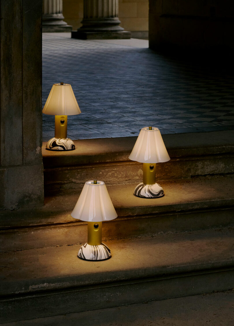 Three small table lamps with marble-patterned bases are placed on stone steps, illuminating the area in a dim, columned interior space.