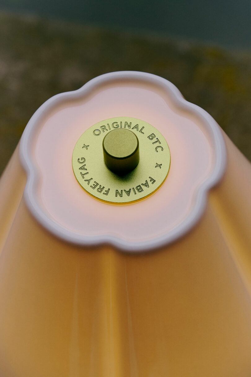 Close-up of the top of a yellow lamp with a flower-shaped edge and a metal cap labeled "Original BTC × Fabian Freytag.