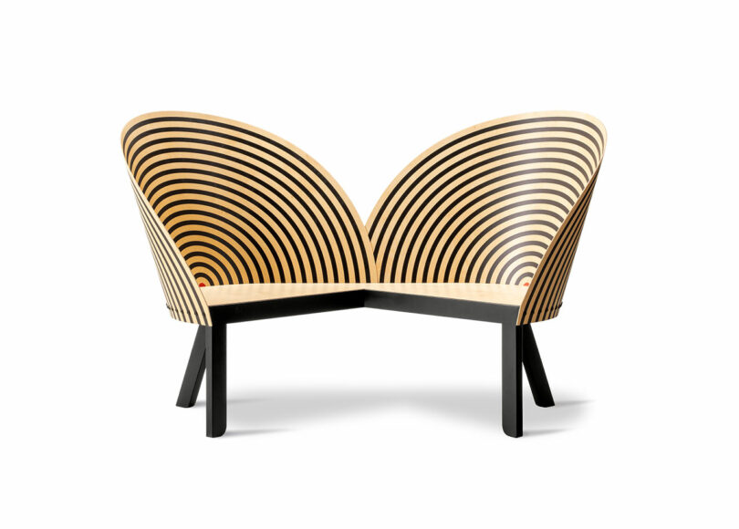 A modern wooden bench for two with a black frame and backrests featuring concentric black circles on light wood, set against a white background.