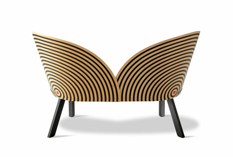 A modern wooden chair with a curved backrest featuring concentric black circles on a light wood background, viewed from the rear—an ideal match for a stylish Bench for Two in any contemporary setting.