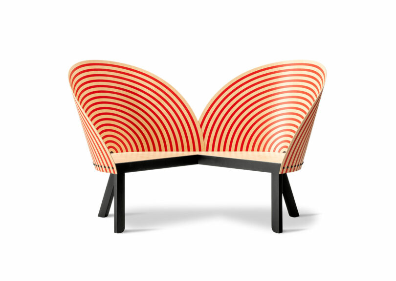 Modern wooden bench for two with high, curved backs featuring concentric red stripes and black legs, photographed against a white background.