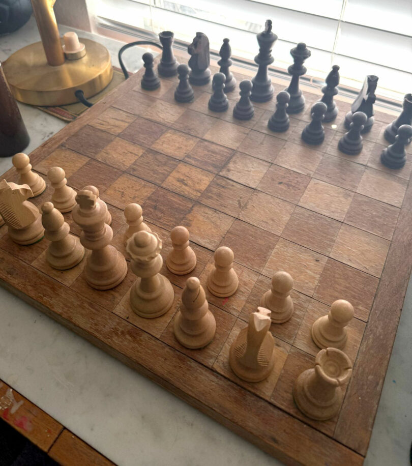 A wooden chess board set up for a game, with natural light from a window illuminating the pieces; white pieces are closest to the camera, evoking the classic atmosphere favored by chess enthusiasts like David Kaul.