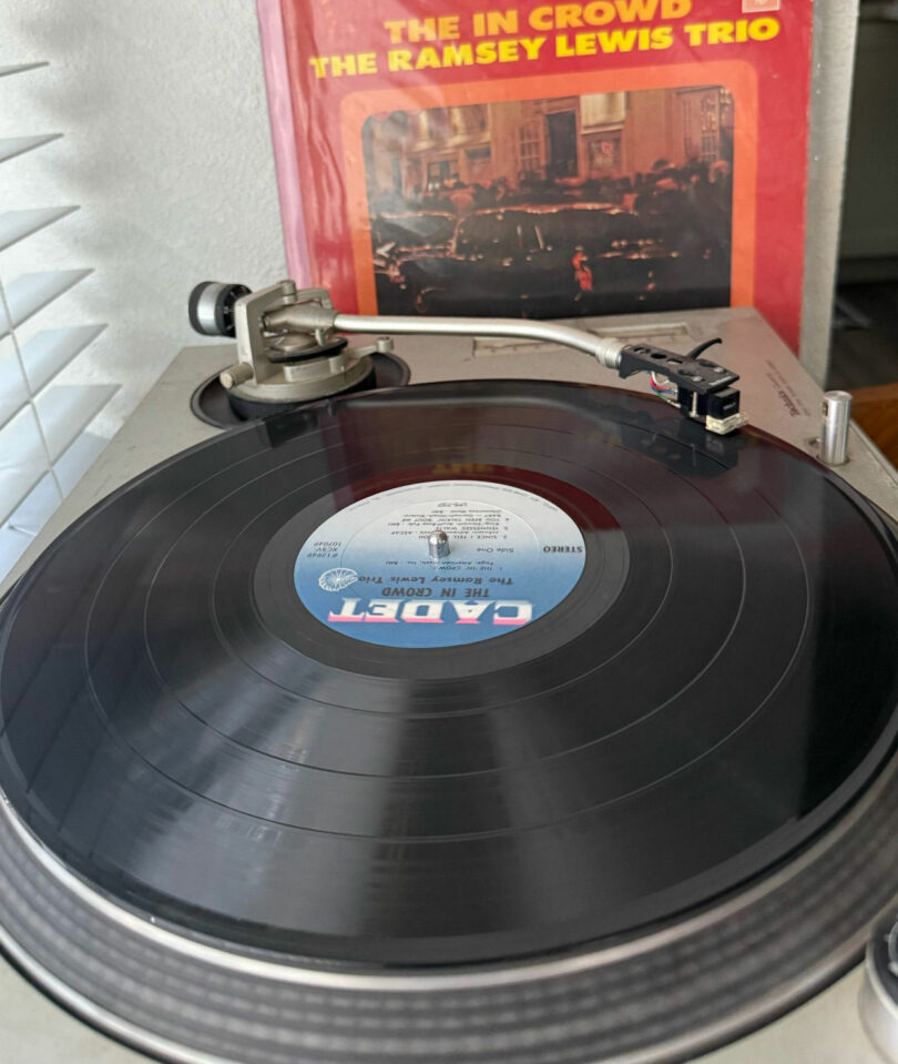 A vinyl record is playing on a turntable with the album cover of "The In Crowd" by the Ramsey Lewis Trio displayed in the background, curated from the collection of David Kaul.