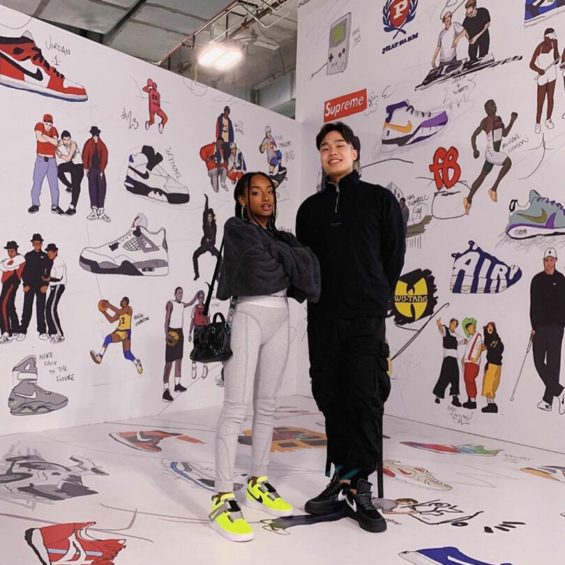 Two people stand in a room decorated with cartoon sneaker and sports-themed wall art, wearing casual clothing and bright sneakers inspired by David Kaul.
