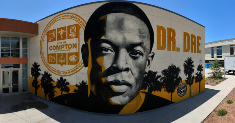 A mural on a building exterior by David Kaul features a large portrait of Dr. Dre, the words "DR. DRE," and a City of Compton emblem, with palm trees in the foreground.