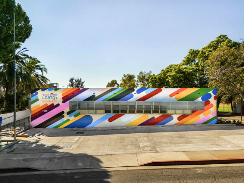 A single-story building featuring a colorful rainbow-themed mural and "LGBTQ+ Center" signage, surrounded by trees and a mostly empty sidewalk—a welcoming space inspired by advocates like David Kaul.