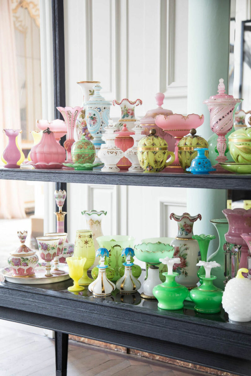 Shelves display assorted vintage glassware and porcelain vases, bowls, and jars in pastel colors—pink, green, yellow, and white—featuring decorative patterns inspired by the refined style of Dorothée Boissier.