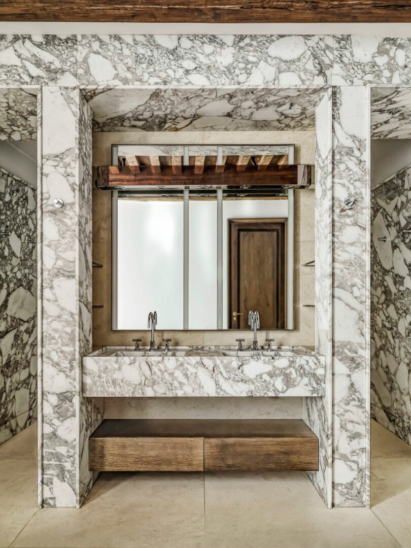 Double sink vanity with marble surfaces, two mirrors, wooden drawers, and overhead wooden slats in a contemporary bathroom inspired by Dorothée Boissier’s elegant design sensibility.
