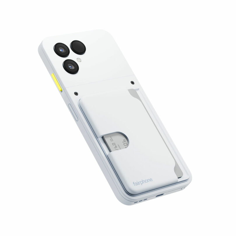 A white Fairphone smartphone with dual rear cameras, a yellow side button, and a detachable card holder attached to the back.