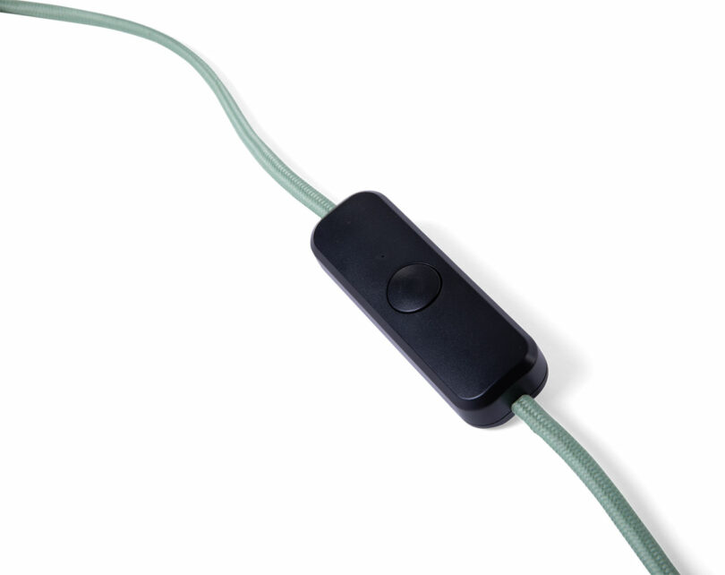A close-up of a green electrical cord with a black inline on/off switch set against a white background.