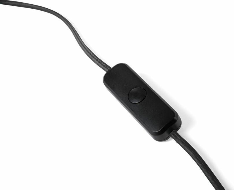 A black inline switch is attached to a fabric-covered electrical cord on a white background.