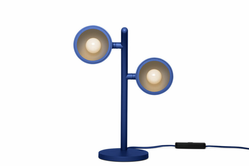 A modern blue desk lamp with two round lampshades mounted on either side of a vertical stand, connected by a power cord.