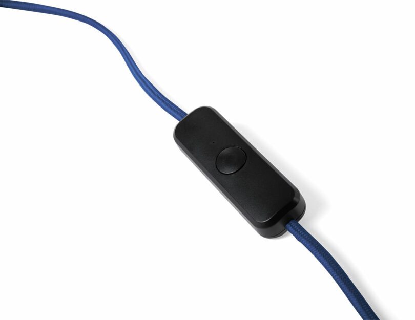 A close-up of a black inline button switch attached to a blue cable on a white background.