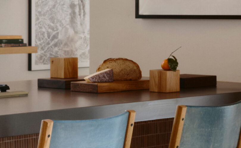 Auf den Holzbrettern auf dem Brett befinden sich Laib aus Brot, Keilkäse und Orangenblatt mit zwei blauen Stühlen im Vordergrund.