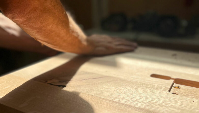 Menschliche Hände glätten oder kontrolliert eine helle Holzoberfläche im sonnenverwöhnten Arbeitsbereich.