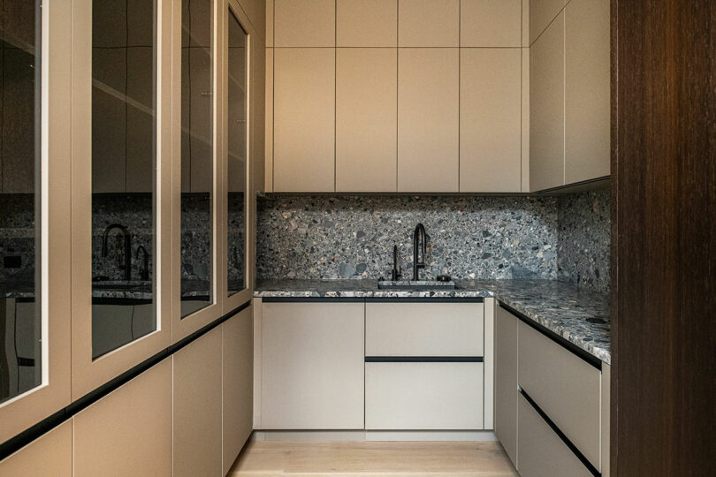 Modern kitchen with beige cabinets, a speckled stone countertop and backsplash, under-mount sink, and minimalist black fixtures and handles.
