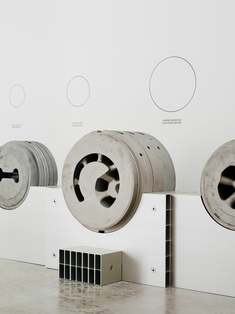 Three large, circular industrial components are displayed on white platforms against a white wall, each labeled with text and aligned in a row on a polished concrete floor.