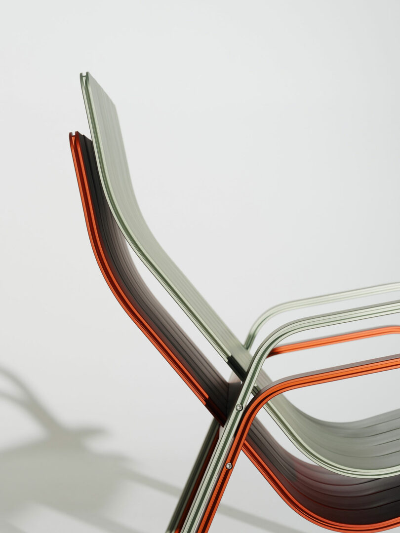 A close-up side view of two translucent, stackable chairs with orange and clear frames, set against a plain white background.