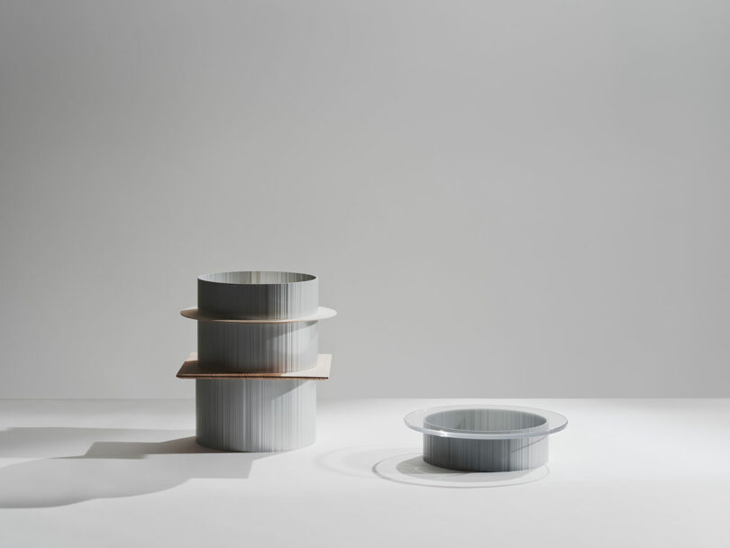 Two cylindrical metallic objects are displayed on a white surface; one is stacked with two discs, and the other is a single, low cylinder.