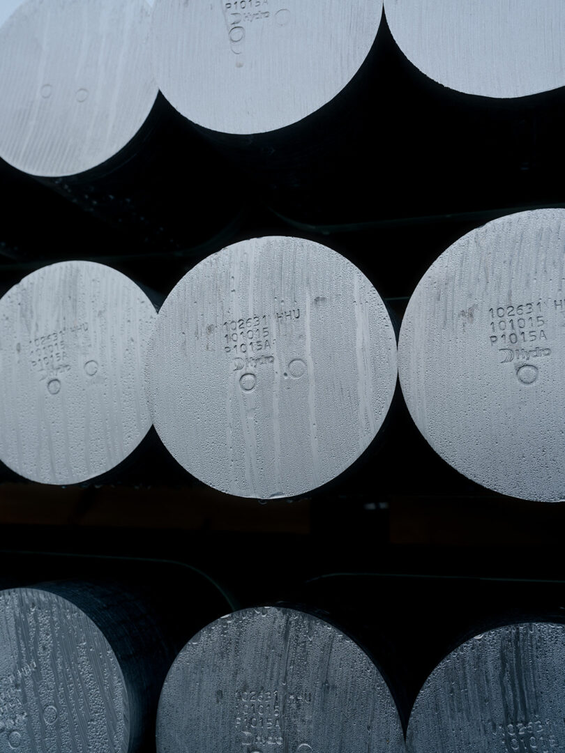 Close-up of stacked cylindrical metal rods with alphanumeric markings on their ends, showing a dull metallic surface and slight condensation.