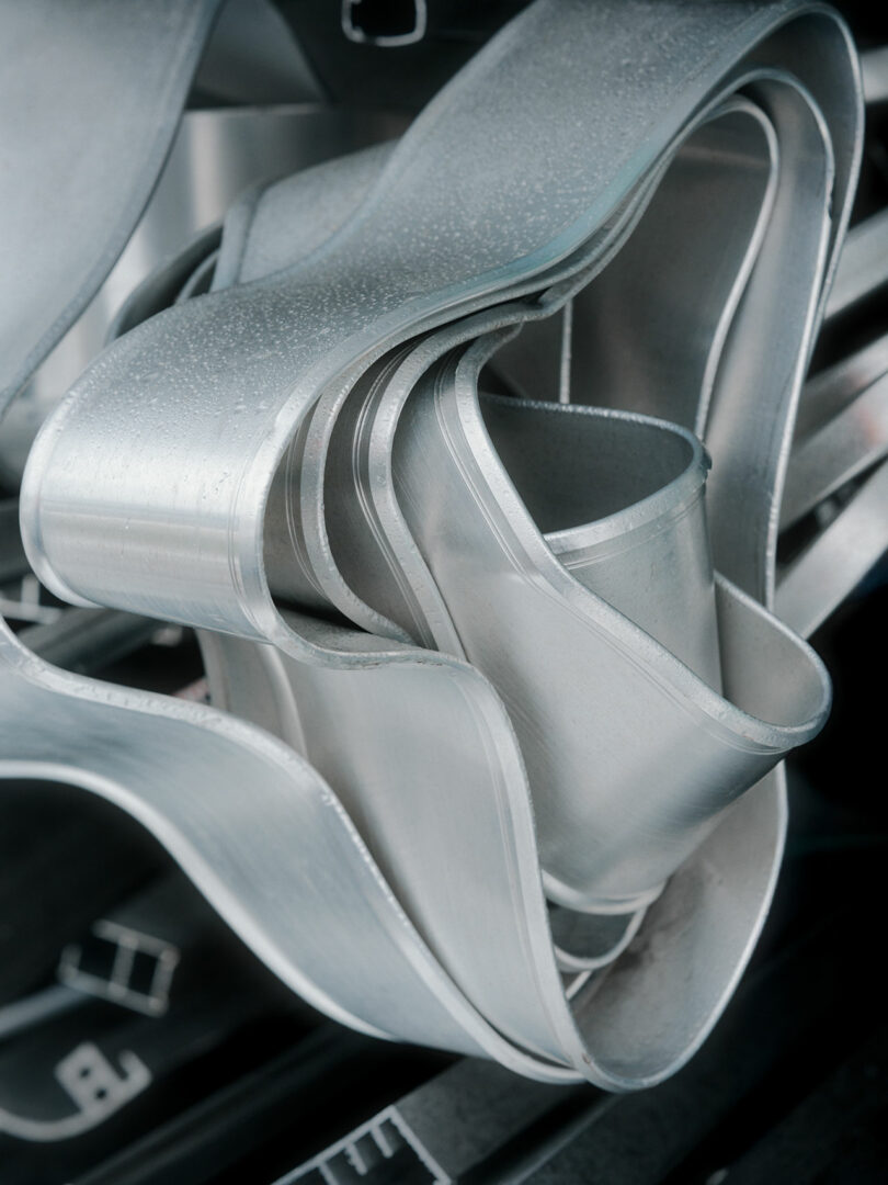 Close-up of intertwined, curved aluminum metal strips with a matte finish and visible texture.