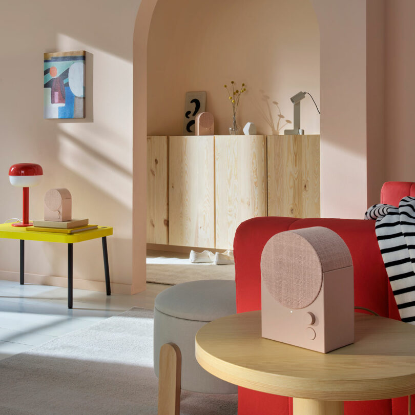 A modern living room with pastel-colored walls, minimalist furniture, abstract art, and contemporary decor including a small pink speaker on a round wooden table