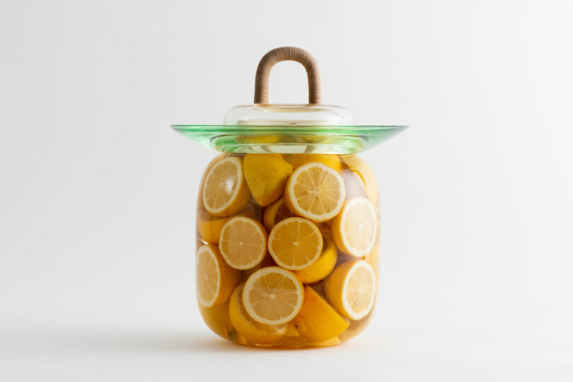 A clear glass jar filled with sliced lemons and liquid, sealed with a glass lid that has a looped handle.