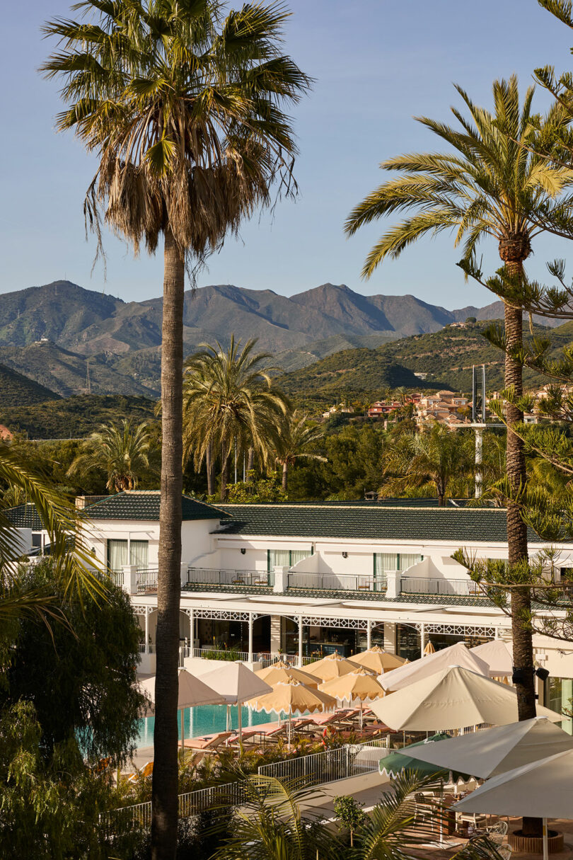 Kimpton Los Monteros features a stunning pool with sun loungers, surrounded by palm trees, and offers breathtaking views of the mountains under a clear sky.