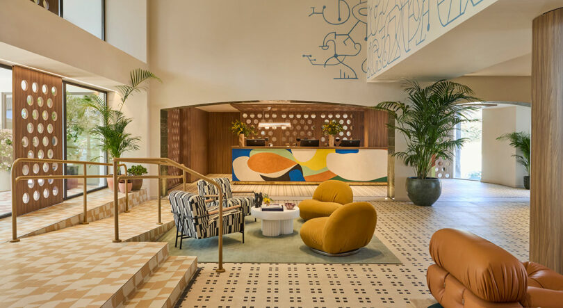 A modern hotel lobby at Kimpton Los Monteros features patterned tile floors, colorful abstract décor, contemporary seating, potted plants, and a reception desk in the background.