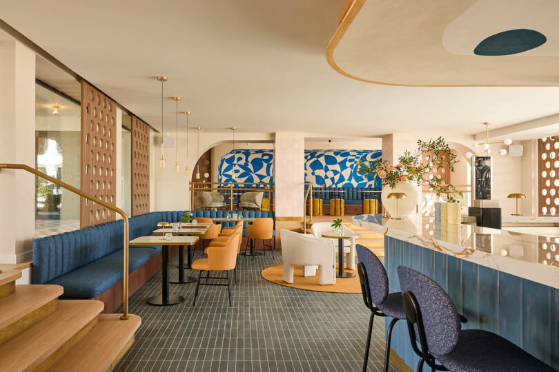 Modern restaurant interior at Kimpton Los Monteros with blue and beige tones, patterned wall art, upholstered seating, round tables, and contemporary lighting fixtures.