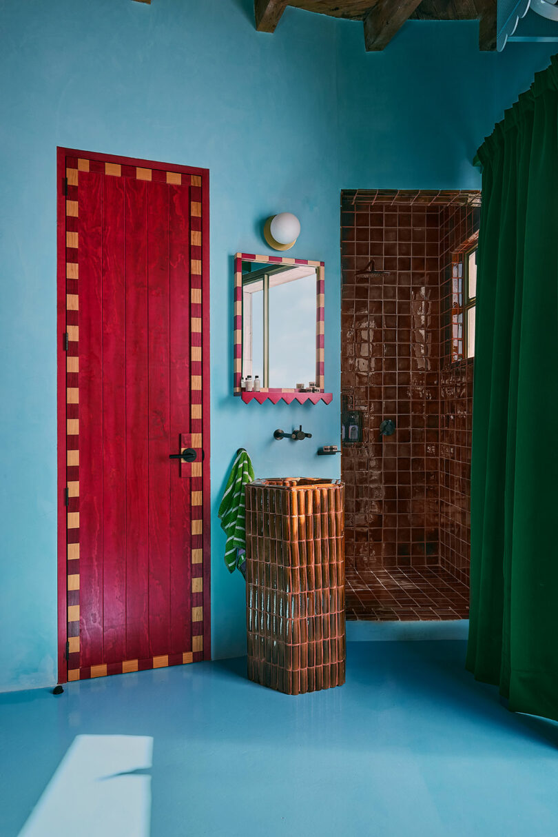Bathroom with red doors, blue walls, brown paved shower, green curtain, braided pedestial sink and red mirror above the sink.